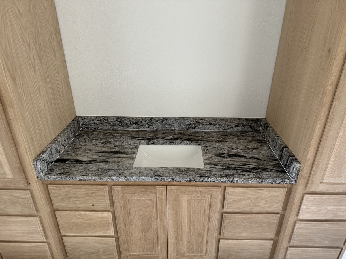 Blue Dunes granite bathroom vanity with undermount sink and light oak cabinets — Central Texas