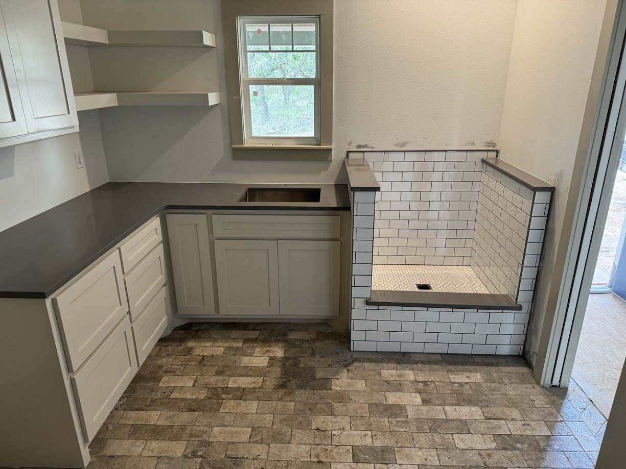 Steel Grey leathered granite kitchen countertops with dark wood cabinets and farmhouse sink — Central Texas