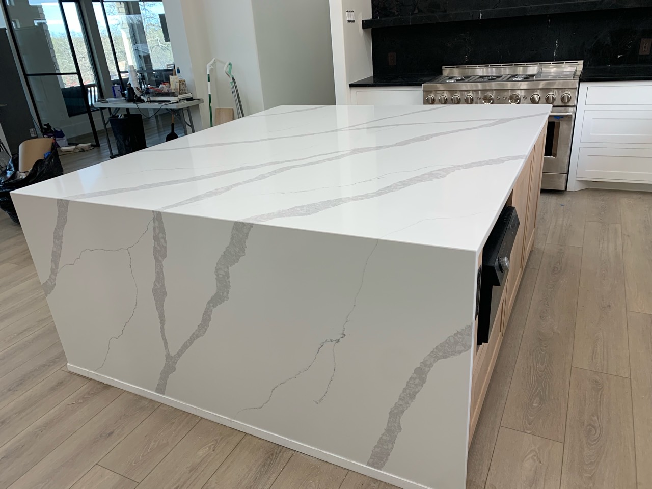 White quartz kitchen island with dramatic grey veining and waterfall edge on light wood cabinetry — Heart of Texas Granite & Marble Central Texas