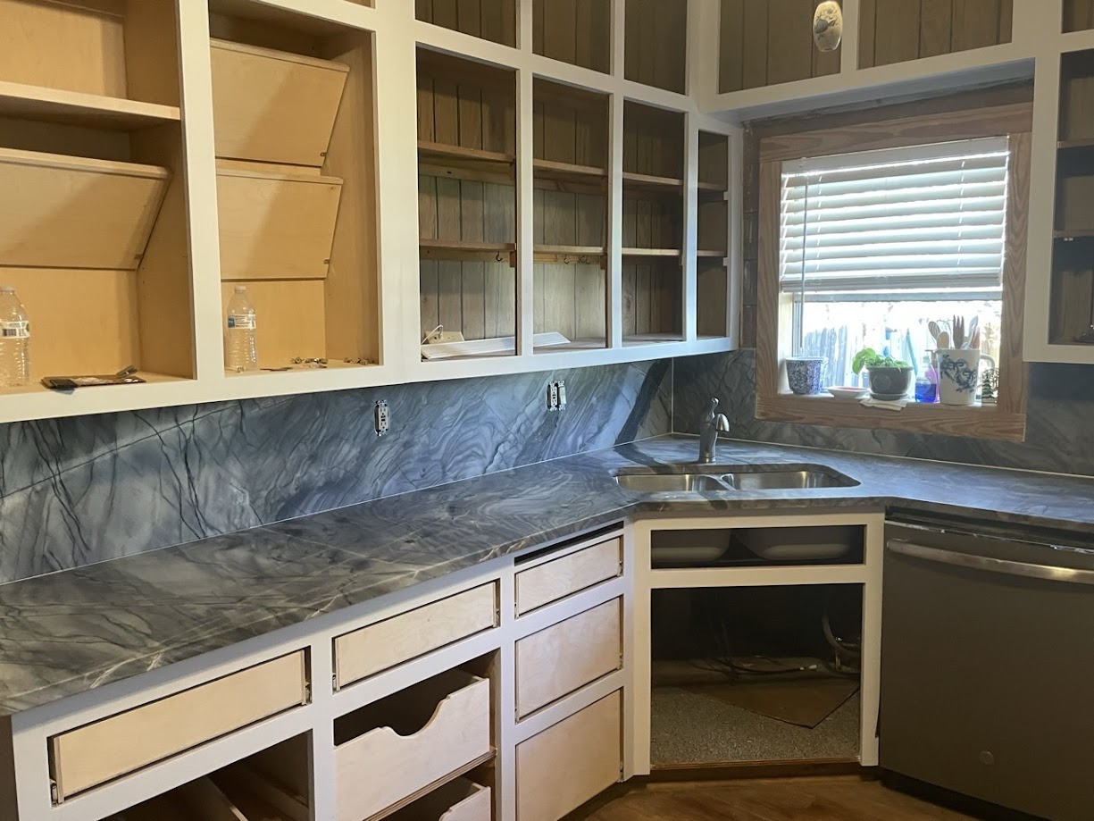 Deep blue grey quartzite kitchen countertops and full slab backsplash with white cabinets and corner undermount sink — Central Texas remodel