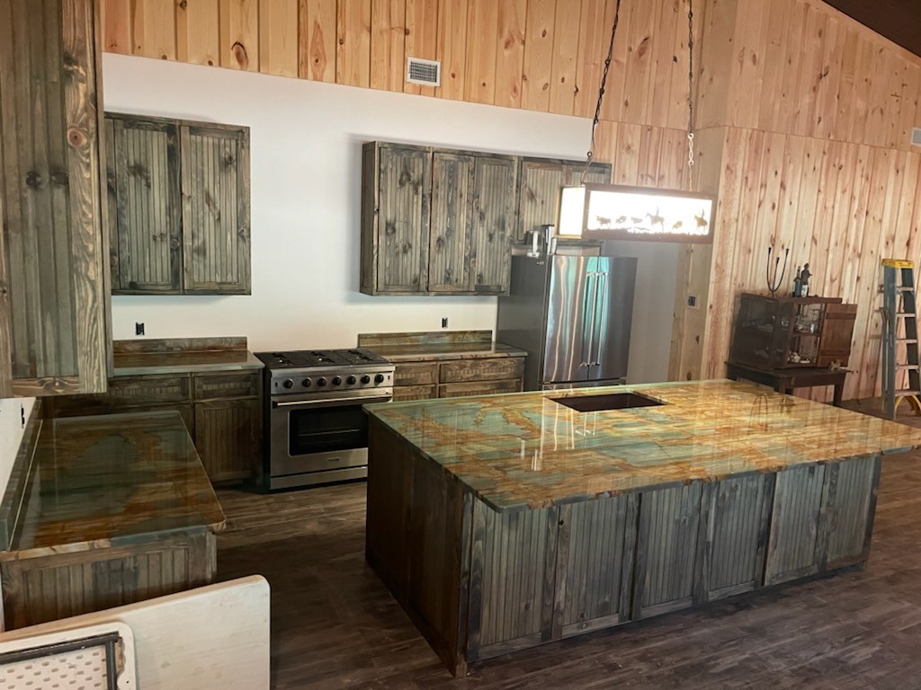 Sauipe quartzite kitchen with dramatic teal green and gold veining on distressed wood cabinets — rustic Texas ranch